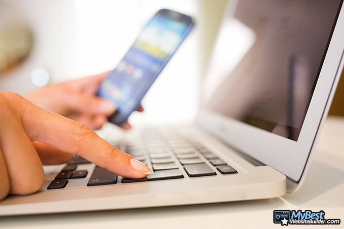 Wix alternatives: woman hands with smart phone and computer keyboard. Wix alternatives: woman hands with smart phone and computer keyboard.